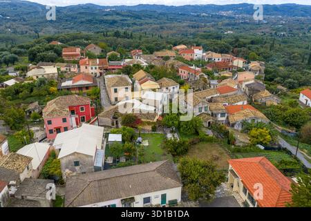 Drohnenblick auf ein traditionelles griechisches Dorf in Korfu aus der Vogelperspektive. Historische Häuser mit roten Ziegeldächern, eingebettet in üppig grünen Wald Stockfoto
