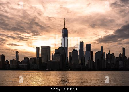 Blick auf die legendäre Silhouette der Stadt vor einem dramatischen Sonnenuntergang über glitzerndem Wasser, der lange Schatten in New York, New York, USA wirft. Stockfoto