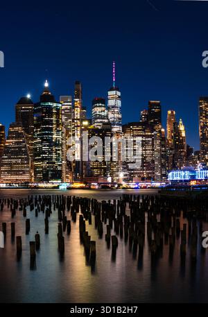 Blick auf glänzende Wolkenkratzer durchdringen den dunklen Himmel, ihre Lichter spiegeln sich im ruhigen Wasser und schaffen einen atemberaubenden Kontrast von Licht und Schatten, New York, USA. Stockfoto