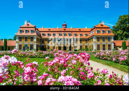 Panoramablick auf das Schloss Rajec Jestrebi an einem sonnigen Sommertag mit blauem Himmel, blühenden rosa Rosen und einem Brunnen vor dem historischen Gebäude. Stockfoto