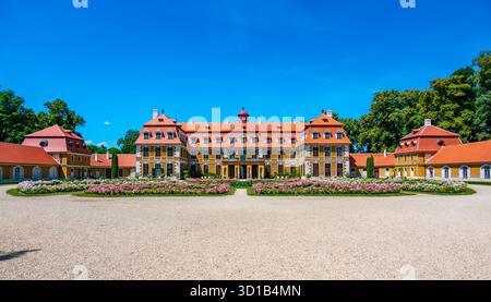 Panoramablick auf das Schloss Rajec Jestrebi an einem sonnigen Sommertag mit blauem Himmel, blühenden rosa Rosen und einem Brunnen vor dem historischen Gebäude. Stockfoto