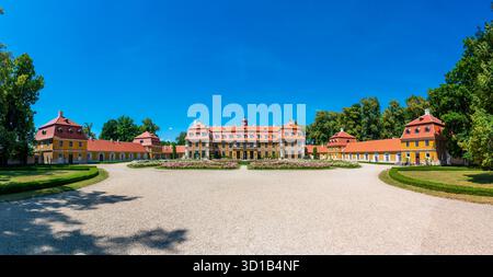 Panoramablick auf das Schloss Rajec Jestrebi an einem sonnigen Sommertag mit blauem Himmel, blühenden rosa Rosen und einem Brunnen vor dem historischen Gebäude. Stockfoto