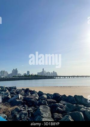 Die Skyline von Panama City von der felsigen Küste und dem Sandstrand von Cinta Costera bei Ebbe unter klarem blauen tropischen Himmel. Stockfoto