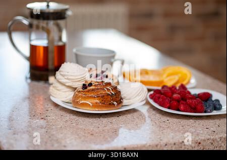 Gemütliche Küchenszene mit Teekanne, Marshmallows, frischen Brötchen und Obst auf einer Arbeitsplatte, warme, heimelige Atmosphäre Stockfoto
