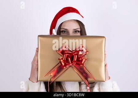 Eine Frau mit Weihnachtsmütze hält ein umhülltes Weihnachtsgeschenk mit roter Schleife Stockfoto