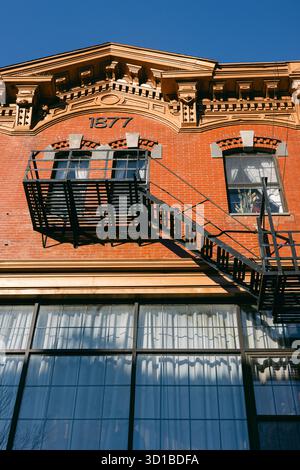 Die historische Backsteinstruktur verfügt über eine markante Feuertreppe und komplizierte Designs vor einem klaren blauen Himmel. Stockfoto