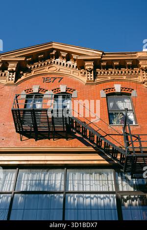 Ein Backsteingebäude verfügt über eine Feuertreppe, die seine historische Architektur vor einem klaren blauen Himmel zeigt. Stockfoto