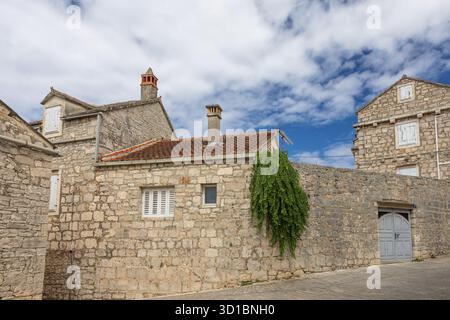 Eine ruhige, mittelalterliche Dorfstraße aus Stein mit Kopfsteinpflasterpfad, Efeu-bedeckten Wänden, einer schweren Holztür und Fensterläden. Heller Himmel en Stockfoto