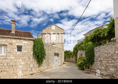 Eine ruhige, mittelalterliche Dorfstraße aus Stein mit Kopfsteinpflasterpfad, Efeu-bedeckten Wänden, einer schweren Holztür und Fensterläden. Heller Himmel en Stockfoto