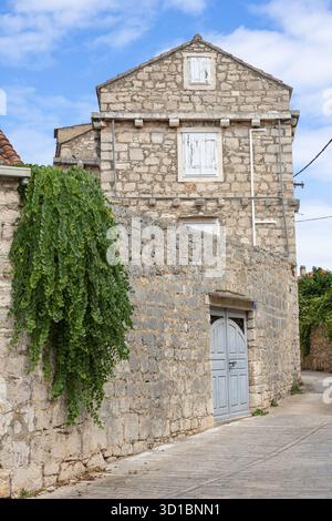 Eine ruhige, mittelalterliche Dorfstraße aus Stein mit Kopfsteinpflasterpfad, Efeu-bedeckten Wänden, einer schweren Holztür und Fensterläden. Heller Himmel en Stockfoto