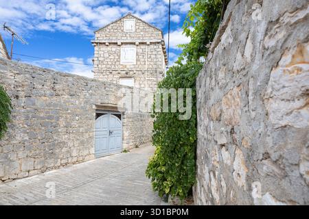 Eine ruhige, mittelalterliche Dorfstraße aus Stein mit Kopfsteinpflasterpfad, Efeu-bedeckten Wänden, einer schweren Holztür und Fensterläden. Heller Himmel en Stockfoto