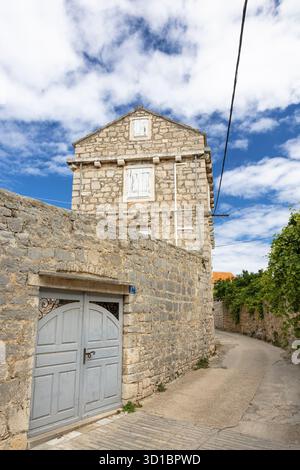 Eine ruhige, mittelalterliche Dorfstraße aus Stein mit Kopfsteinpflasterpfad, Efeu-bedeckten Wänden, einer schweren Holztür und Fensterläden. Heller Himmel en Stockfoto