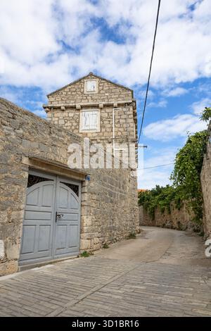Eine ruhige, mittelalterliche Dorfstraße aus Stein mit Kopfsteinpflasterpfad, Efeu-bedeckten Wänden, einer schweren Holztür und Fensterläden. Heller Himmel en Stockfoto