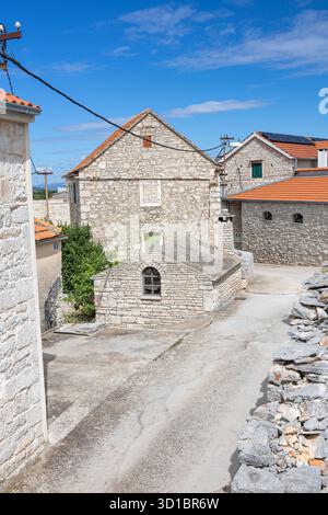 Eine ruhige, mittelalterliche Dorfstraße aus Stein mit Kopfsteinpflasterpfad, Efeu-bedeckten Wänden, einer schweren Holztür und Fensterläden. Heller Himmel en Stockfoto