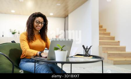 Junge Frau, die im modernen Wohnzimmer an einem Laptop arbeitet Stockfoto