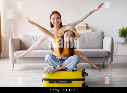 Glückliche Mutter und Tochter genießen einen verspielten Moment auf dem gelben Koffer im Wohnzimmer Stockfoto