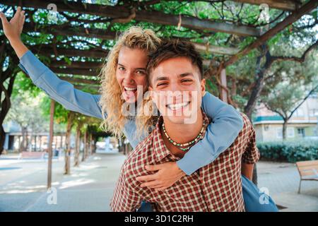 Ein glückliches Paar genießt einen lustigen und unbeschwerten Moment zusammen, wobei ein Partner spielerisch einen Huckepack-Ritt gibt, während beide fröhlich auf den Lächeln Stockfoto