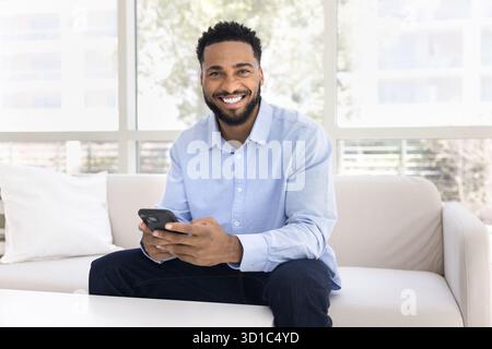 Porträt eines afrikanischen Mannes mit Smartphone auf Sofa Stockfoto