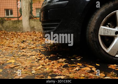 Geparktes Auto mit herabfallendem Herbstlaub auf nassem Asphalt. Saisonale Straßenszene symbolisiert Übergang und ruhige Stimmung. Stockfoto