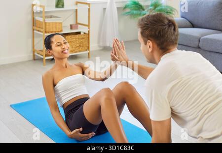 Paar Fitness-Workout zu Hause, Frau macht Sit-ups auf Matte, Mann, der Unterstützung gibt Stockfoto