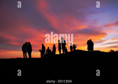Eine Gruppe von Personen mit Silhouette versammelte sich auf einem Hügel während eines lebendigen Sonnenuntergangs mit rosa, orange und violetten Wolken, einer warmen und dramatischen Abendatmosphäre Stockfoto