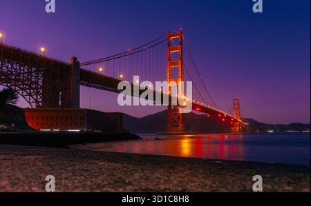Golden Gate Bridge beleuchtet in der Dämmerung mit vibrierenden Reflexen auf ruhigem Wasser, die architektonische Schönheit in der abendlichen Atmosphäre in lebhafter Nacht zum Vorschein bringen Stockfoto