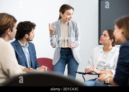 Junge Lehrerin, die Antworten von Schülern unterschiedlichen Alters hört, während sie im Kreis beim Fremdsprachenunterricht sitzt Stockfoto