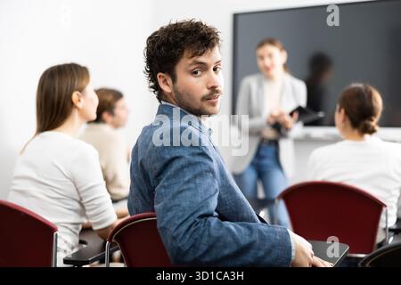 Porträt eines erfolgreichen jungen Mannes, der an Sprachkursen mit einer Gruppe von Menschen im Klassenzimmer teilnimmt Stockfoto
