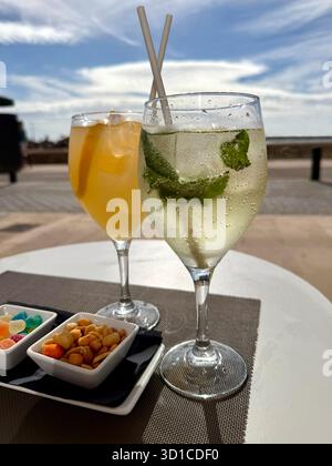 Nahaufnahme von zwei erfrischenden Cocktails, einem Mojito mit Snacks, serviert auf einem Tisch am Meer unter teilweise bewölktem Himmel Can pastilla mallorca Stockfoto