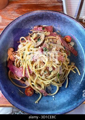 Flachbild-Schüssel mit Spaghetti Carbonara mit Speck, Kirschtomaten, Kräutern und geriebenem Käse, serviert in rustikaler Keramikschale auf Holztisch mallorca Stockfoto
