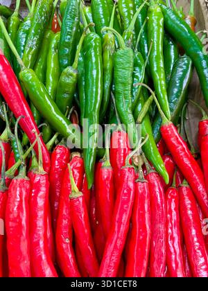 Aus nächster Nähe sehen Sie frische rote und grüne Chili-Paprika, die an einem Marktstand in einer farbenfrohen und lebhaften Ausstellung zusammengestapelt sind Stockfoto
