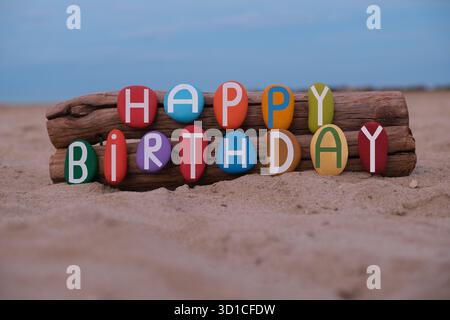 Kreative Happy Birthday-Botschaft mit handgemalten mehrfarbigen Steinbuchstaben am Strand Stockfoto