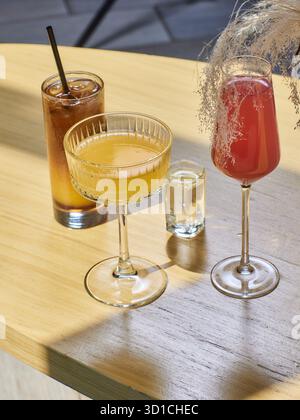 Cocktails auf dem Tisch. Verschiedenfarbige Getränke in verschiedenen Gläsern auf dunklem Holztisch über verschwommenem Restauranthintergrund. Barkonzept, Alkohol Stockfoto