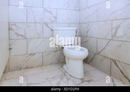 Die Toilette verfügt über eine elegante weiße Toilette vor eleganten Marmorfliesen, die Hygiene betont. Stockfoto