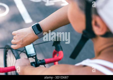 Nahaufnahme einer Radfahrerin, die Smartwatch während der Fahrt im Freien auf markiertem Radweg benutzt Stockfoto