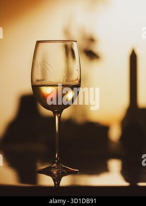 Details mit geringer Schärfentiefe (selektiver Fokus) mit einem Glas Weißwein auf einem Tisch in einem dunklen Raum mit Hintergrundbeleuchtung. Stockfoto