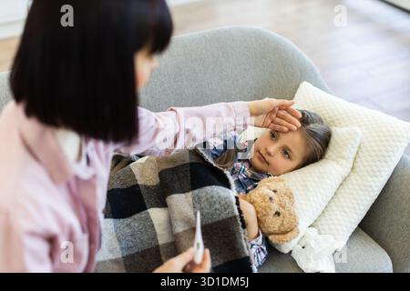 Mutter überprüft die Temperatur ihrer kranken Tochter zu Hause Stockfoto
