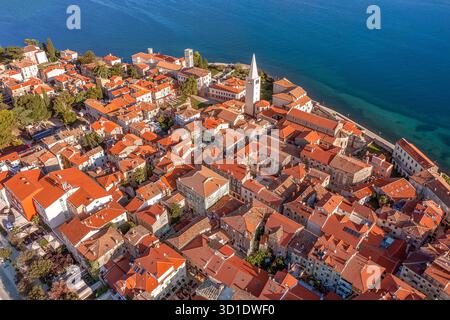 Aus der Vogelperspektive stürzen sich die Terrakotta-Dächer in Richtung der schimmernden Adria, unterbrochen von der majestätischen Spitze der Euphrasianischen Basilika, Poreč, Istrien Stockfoto