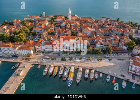 Blick aus der Vogelperspektive auf die Terrakotta-Dächer stürzen sich hinunter und treffen auf das türkisfarbene Wasser, wo farbenfrohe Boote die Küste in der Nähe der berühmten Euphrasianischen Basilika säumen. Stockfoto