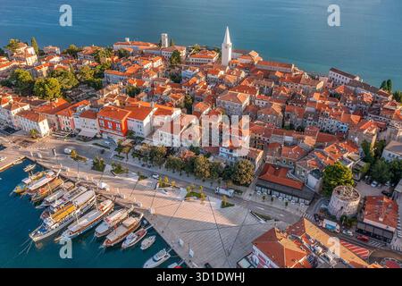 Aus der Vogelperspektive stürzen sich die Terrakotta-Dächer herunter und treffen auf das azurblaue Meer, während der Turm der ikonischen Euphrasianischen Basilika den Himmel durchbohrt, Poreč, Istrien Cou Stockfoto