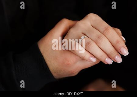 Eine Nahaufnahme zeigt die Hände eines Paares, während ein Verlobungsring aus Weißgold präsentiert wird, der Liebe, Engagement und einen herzlichen Vorschlag symbolisiert. Stockfoto