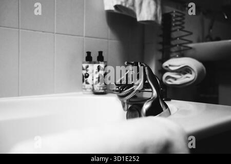 Ein Schwarzweiß-Foto fängt die ruhige Atmosphäre einer Badewanne mit Klauenfuß ein, wobei die Beine einer Person teilweise in Wasser getaucht sind und so ein Gefühl schaffen Stockfoto