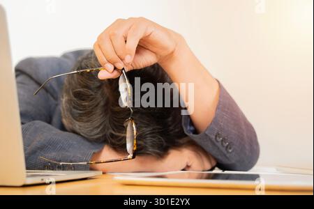 Ein erwachsener Geschäftsmann macht ein Nickerchen am Schreibtisch, Stress und Ermüdung in der Nacht im Büro und Kopfschmerzen am Computer für den Projektermin. Stockfoto