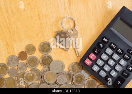 Finanzausweis mit Münzen, Hausschlüssel und Taschenrechner auf Holztisch. Finanzen und Schlüssel, Geld für Hauskonzepte sparen. Draufsicht. Stockfoto