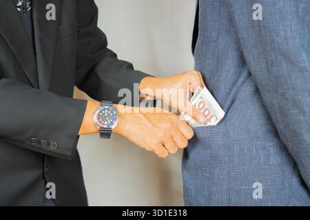 Die Hand wirft US-Banknoten in die Tasche eines Mannes in Anzug und Krawatte, der vor ihm steht. Bestechungsgelder zu geben. Korruption Stockfoto