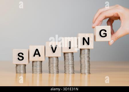 Eine Nahaufnahme einer Frauenhand, die Holzwürfel hält, die Schreibweise auf dem Stapel einer Münze speichert. Geldplanung und Geschäftsfinanzanalyse. Stockfoto