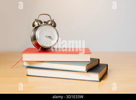 Vintage-Wecker auf einem Stapel Bücher auf einem Holztisch. Weißer Hintergrund und leerer Kopierbereich für Editor-Text. Stockfoto