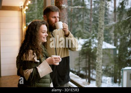 Kaukasische junge Frau und Mann genießen heiße Getränke auf dem Winterbalkon Stockfoto