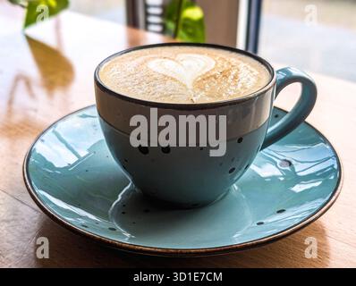 Nahaufnahme eines Cappuccino oder Latte mit herzförmiger Schaumkunst in einer türkisfarbenen Tasse Stockfoto