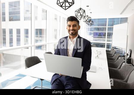 Glücklicher erfolgreicher junger indischer Firmenbesitzer, der einen Laptop hält Stockfoto